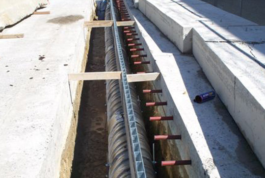 Concrete construction site with exposed rebar and a drainage system installation in progress.