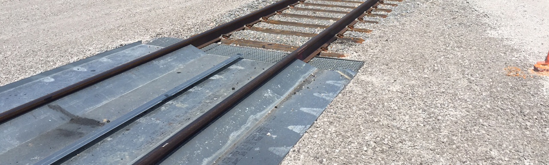 Railroad tracks running through a gravel-covered area with utility poles and a clear sky in the background.