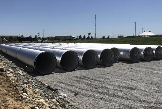 Several large metal pipes aligned on a gravel area under a clear blue sky.