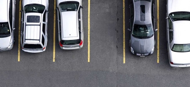 Top-down view of five cars parked in a row in a parking lot, with visible parking lines and empty space to the right.