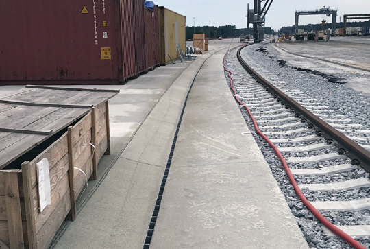 Train tracks beside a shipping container yard, with wooden crates and containers in the background.