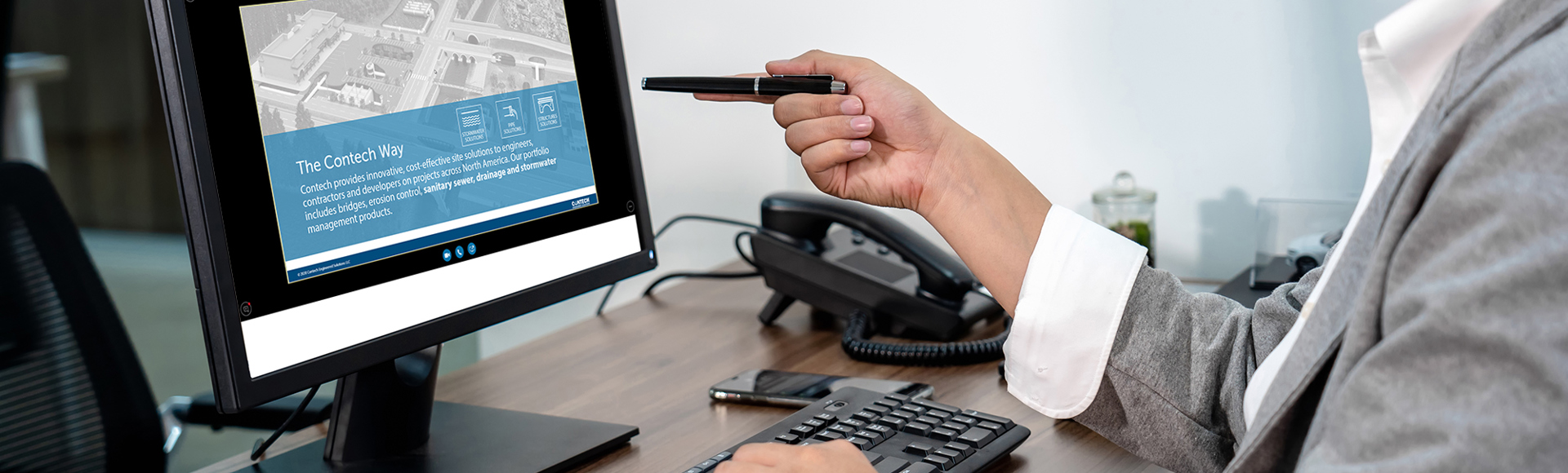 A person in a suit points at a computer screen displaying a website in an office setting.