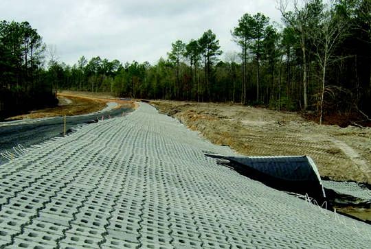Hexagonal concrete blocks form a pathway on a construction site, with surrounding trees and a partially clear sky.
